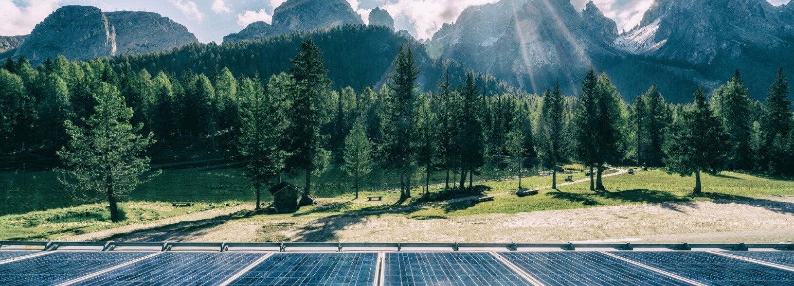 Panele fotowoltaiczne na tle lasu iglastego i gór