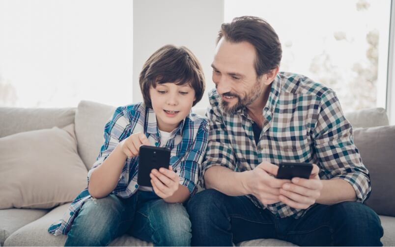 Ojciec i syn siedzą na kanapie i spoglądają na ekran telefonu